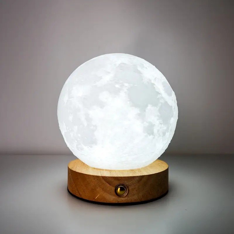 Lampe lune blanche et réaliste posée sur une base en bois ronde avec interrupteur, éclairant une pièce sombre.