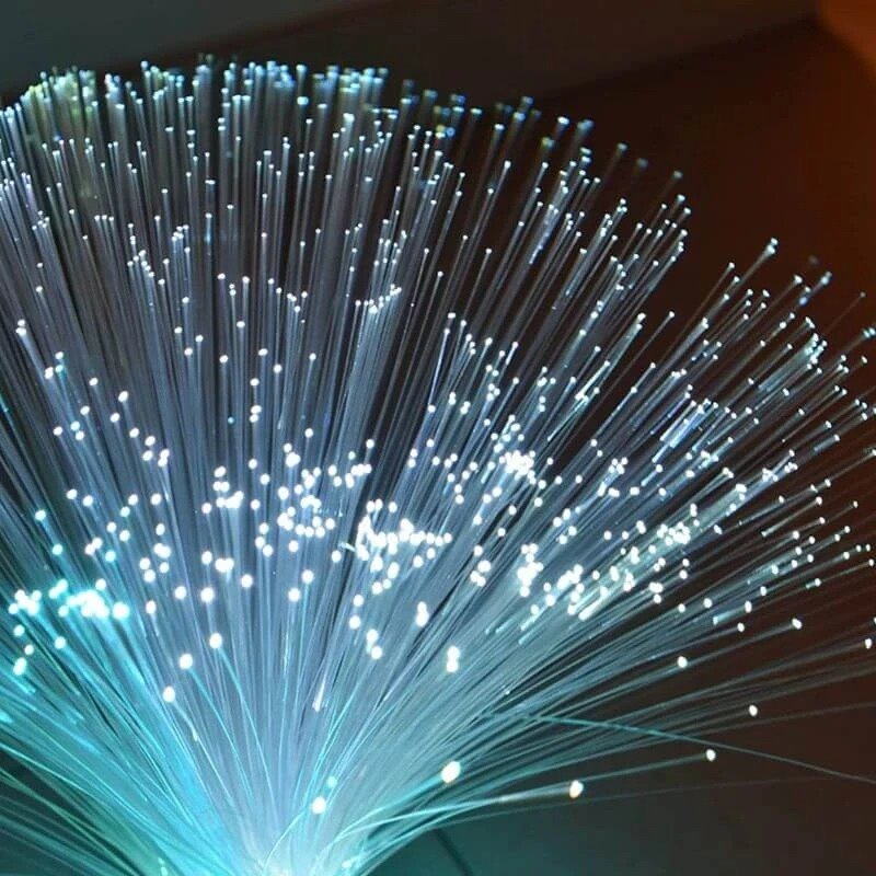 Gros plan sur les faisceaux de fibres optiques d'une lampe constellation, avec des points lumineux blancs sur un fond bleu.
