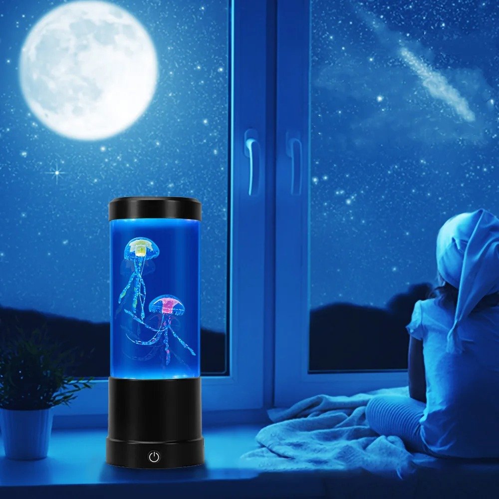 Lampe aquarium méduses bleues posée sur le rebord d'une fenêtre avec une personne coiffée d'un bonnet regardant la pleine lune et le ciel étoilé
