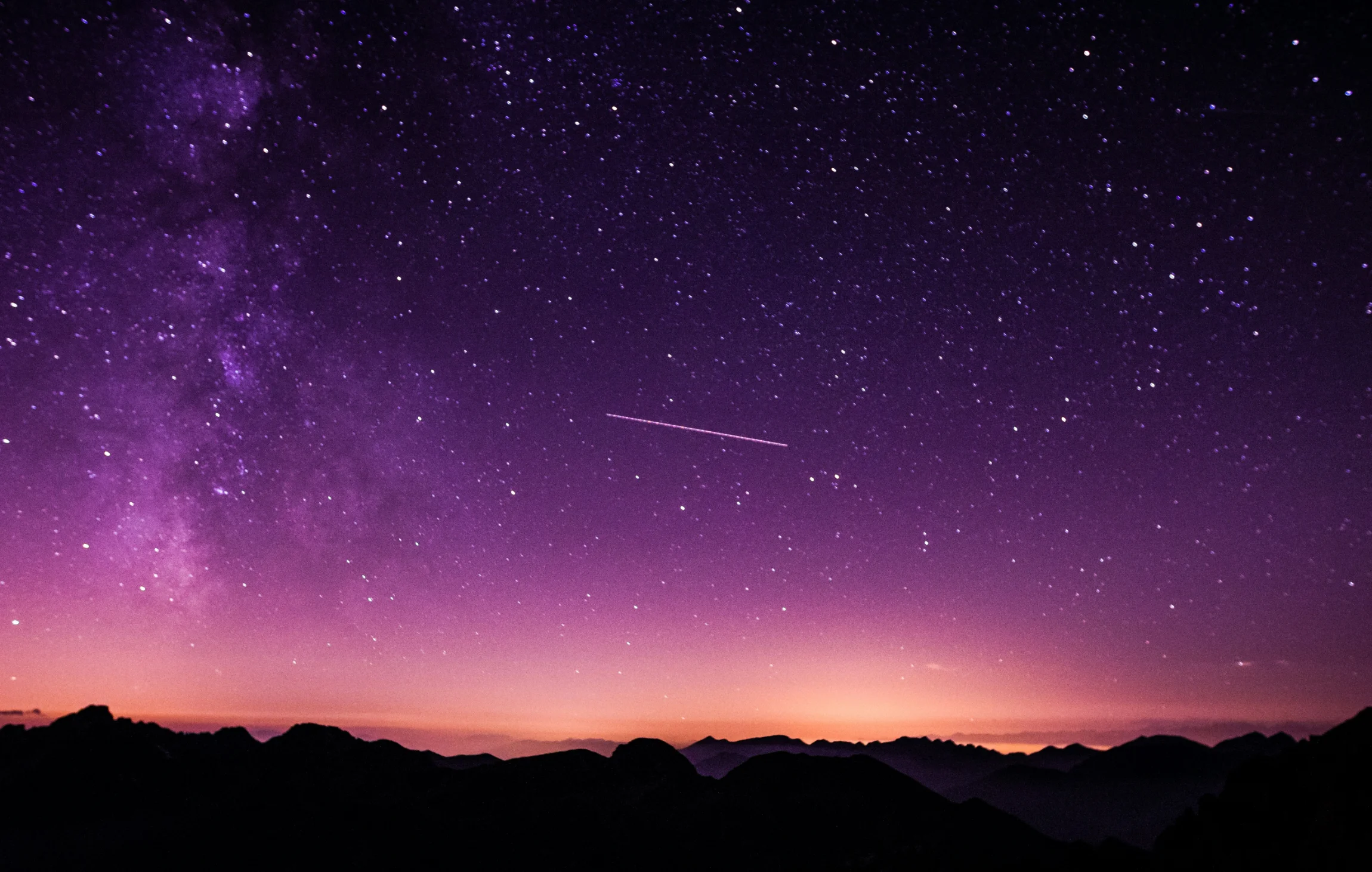 Vibrant night sky with the Milky Way and a shooting star over silhouetted mountains at dusk